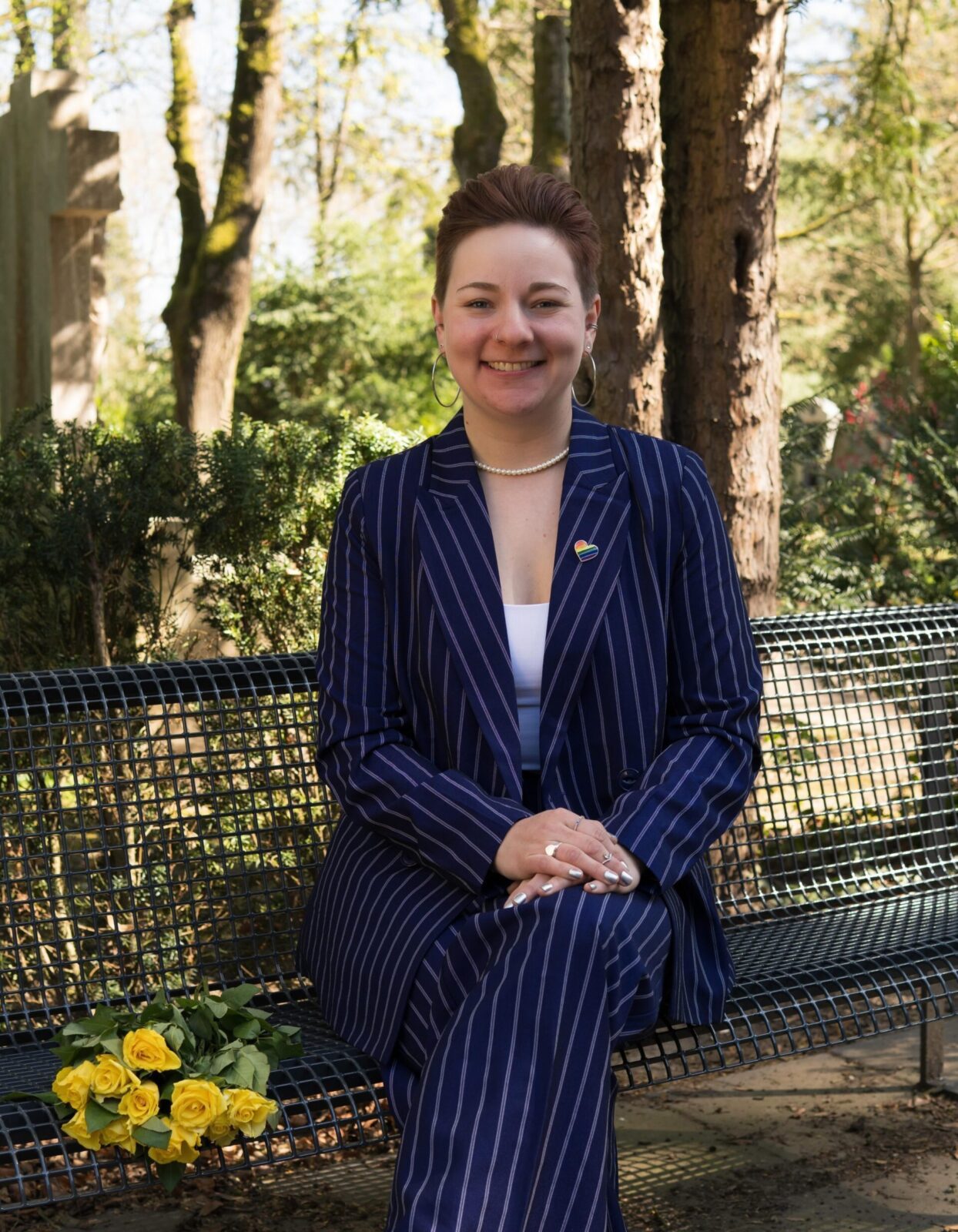 Rednerin Caro sitzt auf einer Bank auf einem Friefhof und lächelt in die Kamera