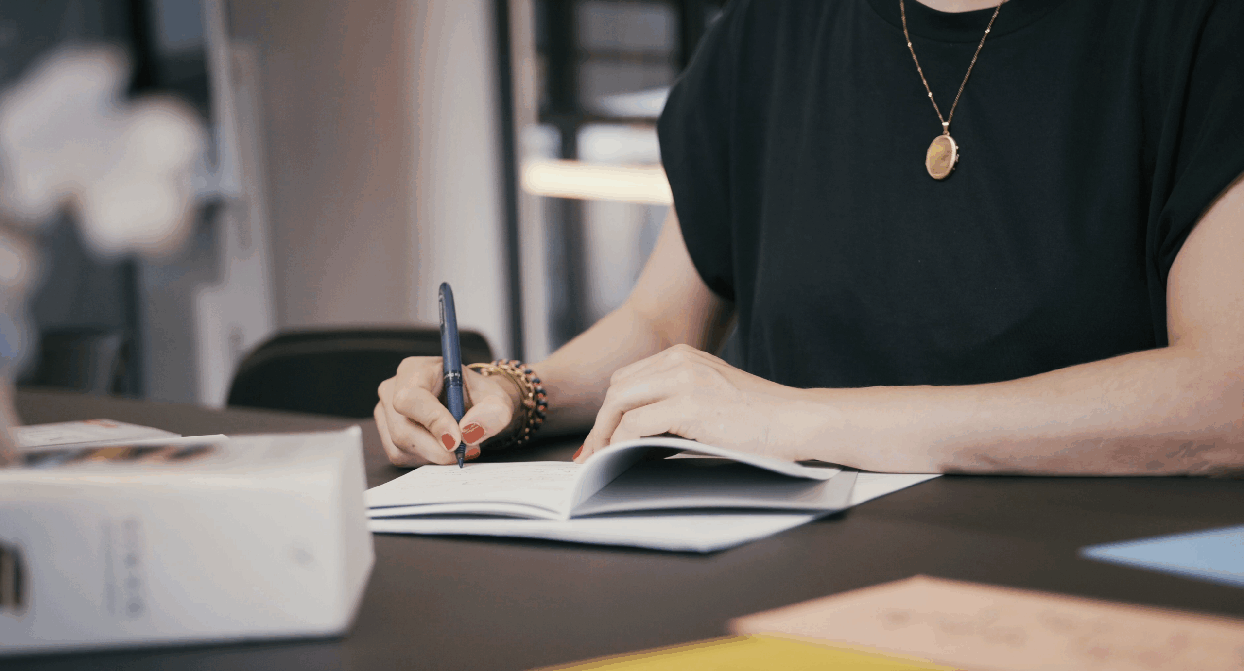 Trauerrednerin Weiterbildung Ein Schreibtisch mit einem Notizheft von Wer Du warst was geöffnet ist und von Gründerin Carina Fritz deren Hände und Oberkörper abgebildet sind beschrieben wird