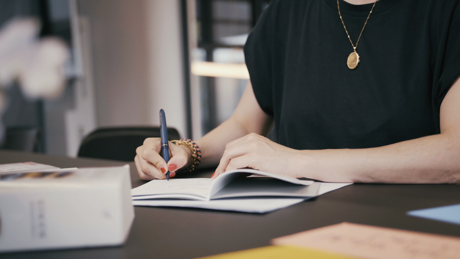 Trauerrednerin Weiterbildung Ein Schreibtisch mit einem Notizheft von Wer Du warst was geöffnet ist und von Gründerin Carina Fritz deren Hände und Oberkörper abgebildet sind beschrieben wird