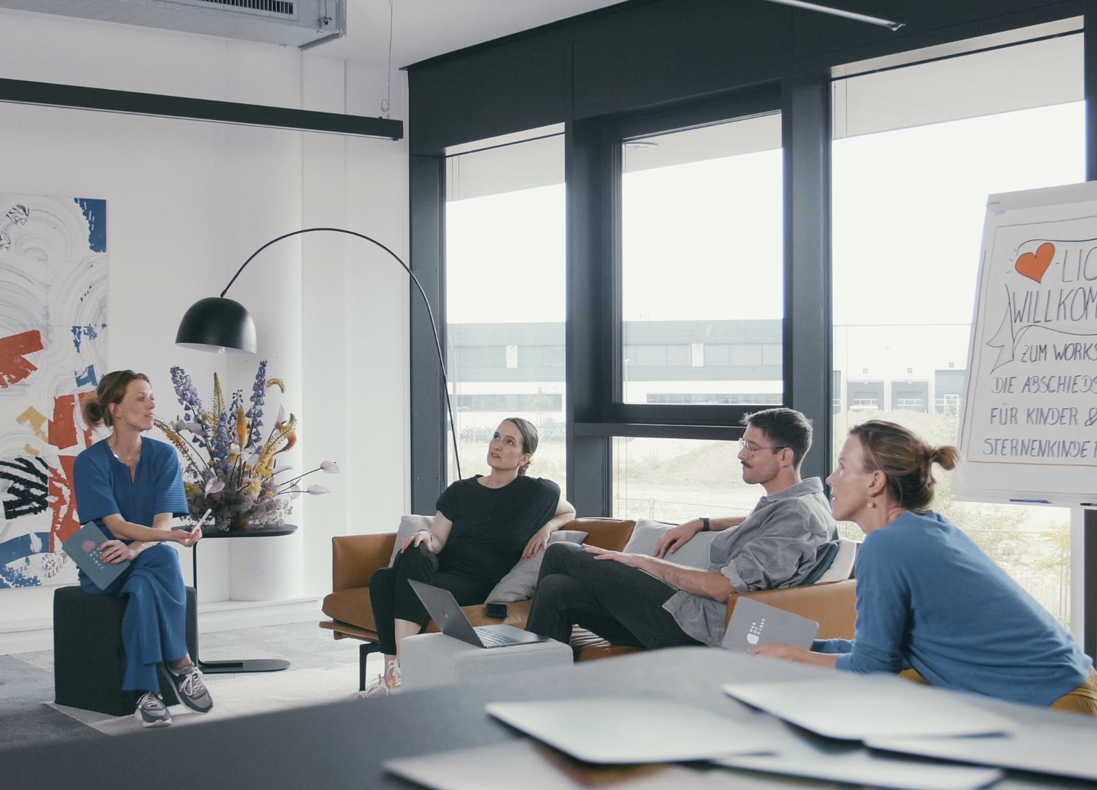 Alle Wer DU Warst Masterclass Expert*innen sitzen zusammen im Ship in Köln und unterhalten sich Mel Breese Carina Fritz Benni Bauerdick und Gunda Tibelius sind im Bild im Hintergrund ein Flip Chart auf dem Steht Herzlich willkommen zum Workshop Abschied nehmen von Kindern und Sternenkindern