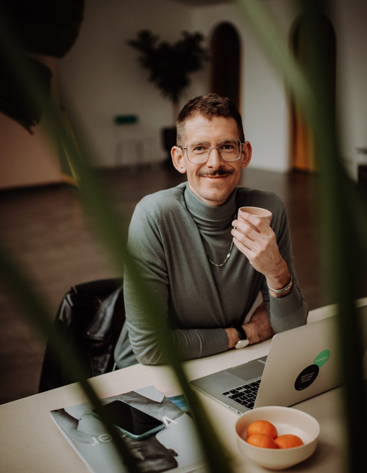 Benni Bauerdick unser Experte für Sprechen Stimme und Souveränes Auftreten sitzt an einem Schreibtisch mit einem Kaffee in der Hand und schaut in die Kamera