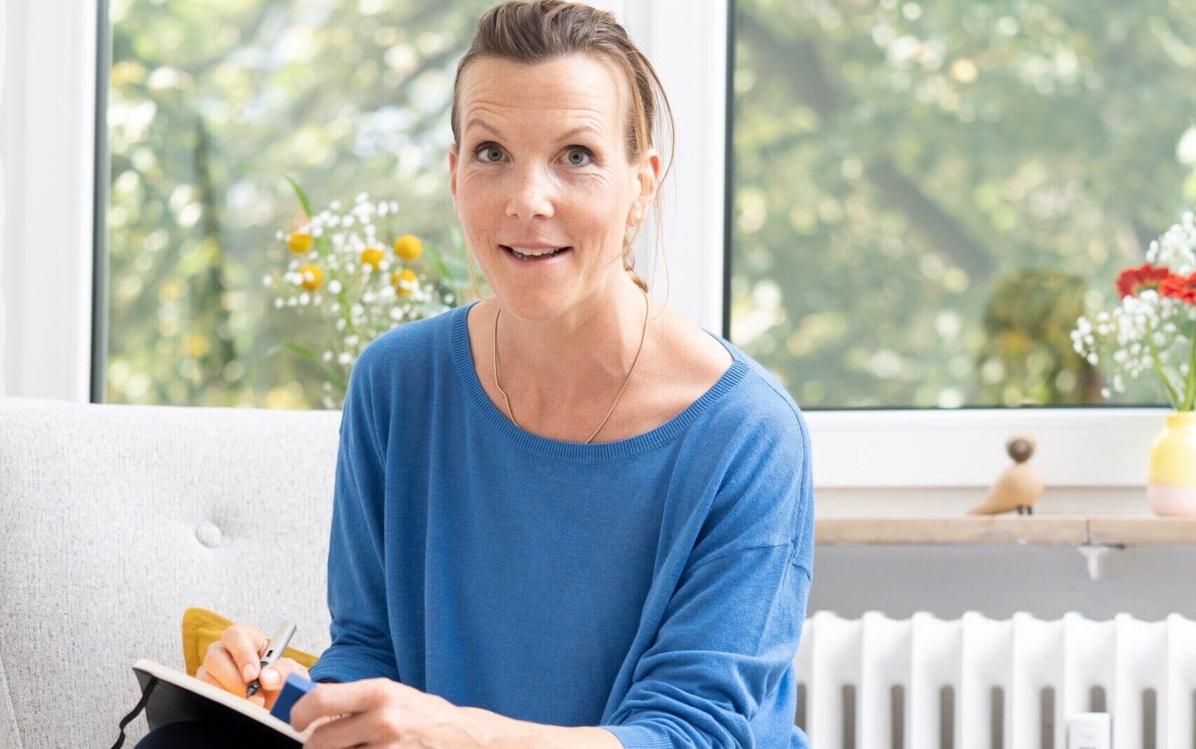 Gunda Tibelius sitzt auf einem Sofa und schaut in die Kamera.