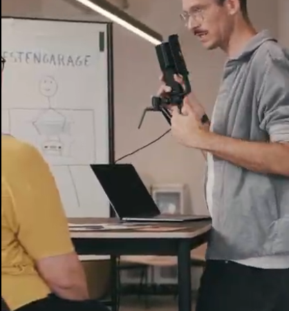 Stimme Sprechen Souveränität Benni Bauerdick Benni Bauerdick steht mit einem Mikro zur Podcast Aufnahme vor einem Tisch im Workshop für Stimme Sprechen und Souveränität in der Trauerbranche