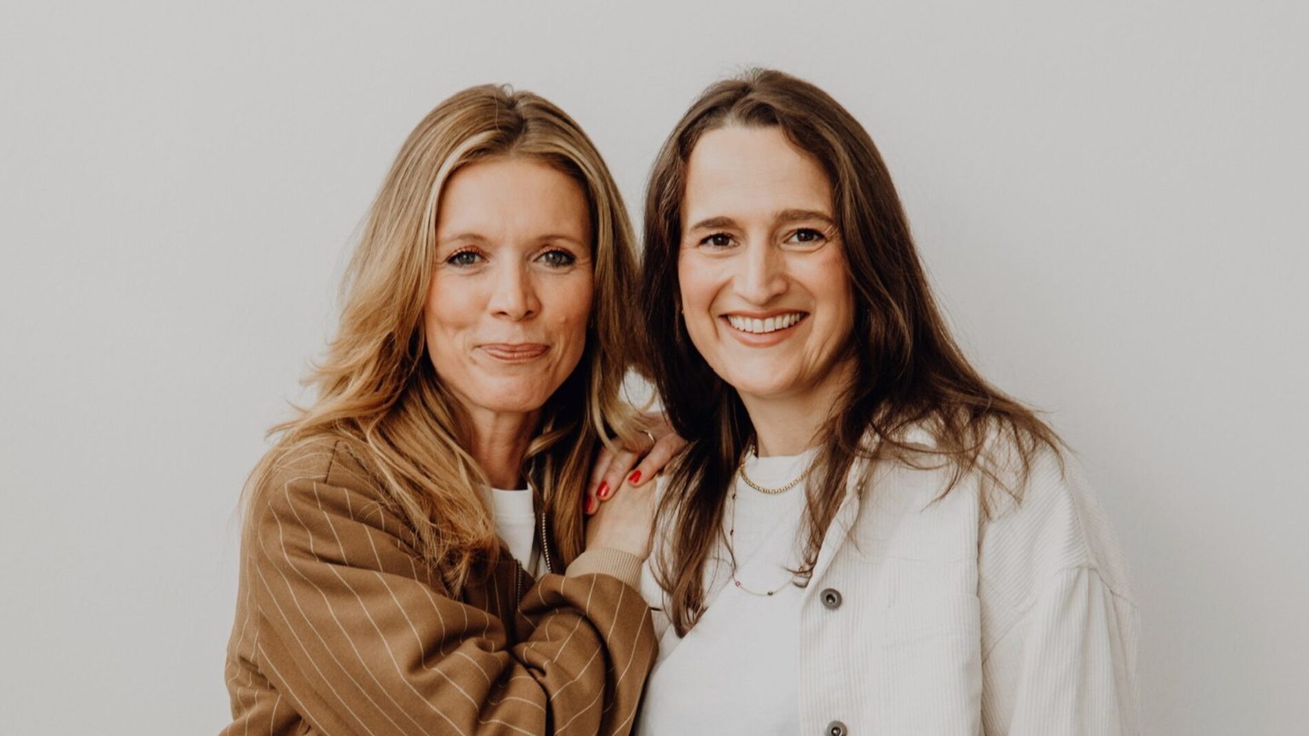 Trauerredner-finden-WER-DU-WARST-Gründerinnen-Carina-Fritz-Mel-Breese4 Trauerrednerinnen und Gründerinnen von Wer Du Warst Carina Fritz und Mel Breese stehen vor der Kamera in freundschaftlicher Umarmung und lächeln in die Kamera