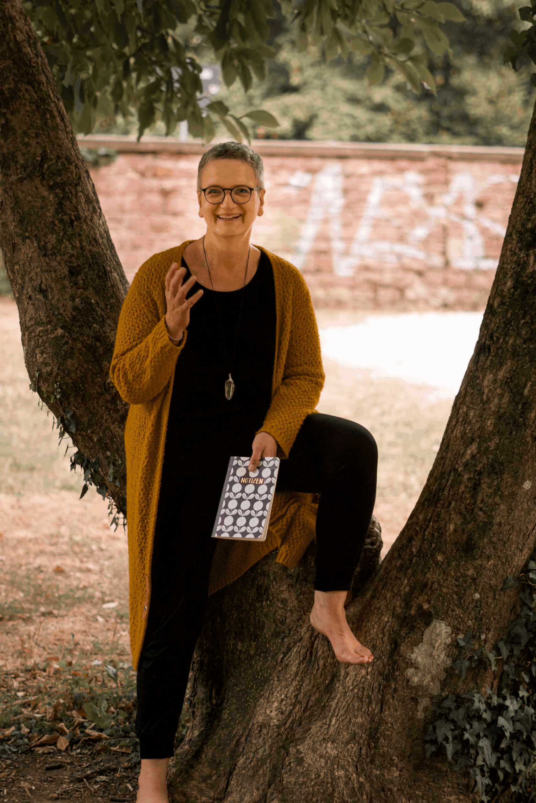 Expertin für Abschied von Kindern und Sternenkindern Trauerbegleiterin Claudia Hahn sitzt auf einem Baum und gestikuliert in die Kamera