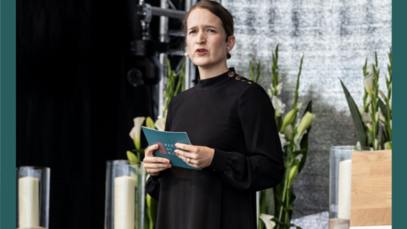 image Gründerin Carina bei einer Trauerrede mit Moderationskarten von Wer Du warst in den Händen sie hat ein Headset Mikrofon auf und man sieht die von vorn beim Reden