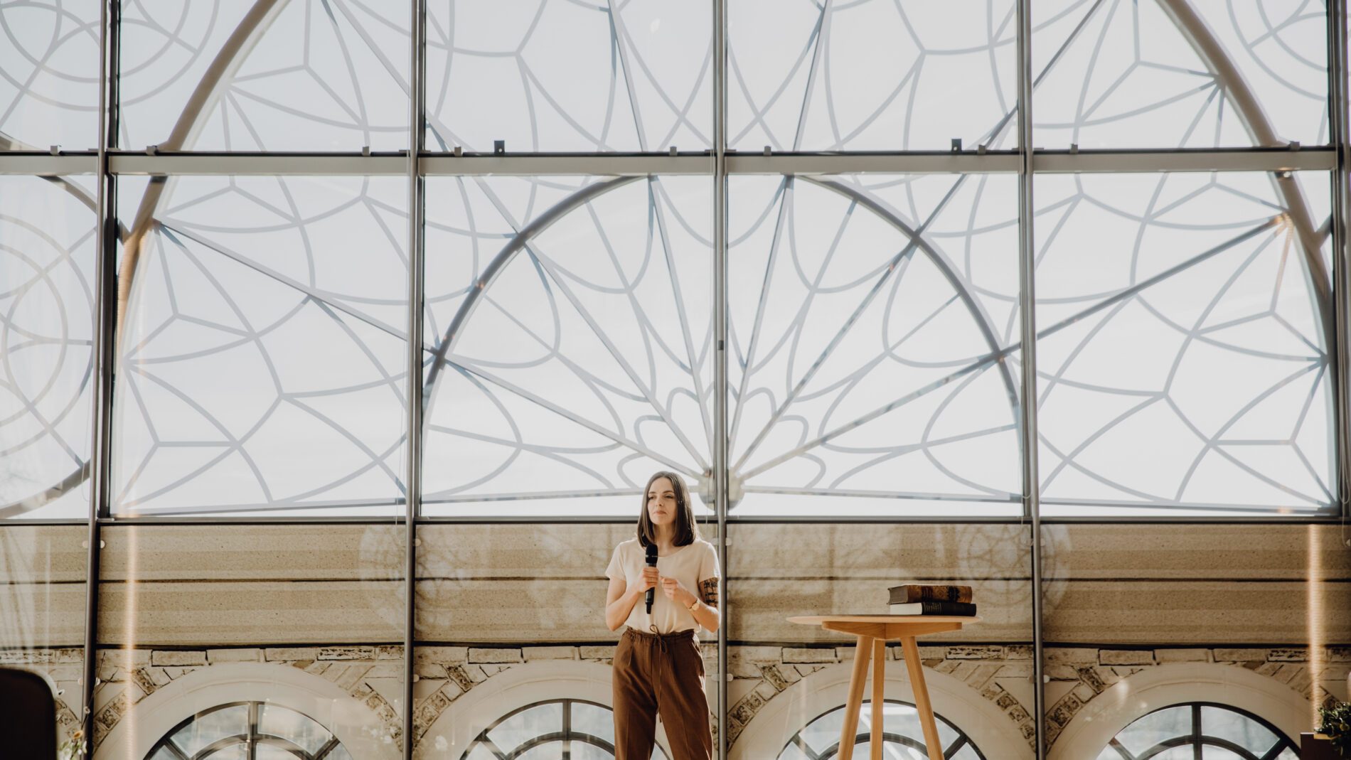 Trauerrednerin von WER DU WARST steht vor prunkvollem Fenster in der Flora und redet in ein Mikrofon
