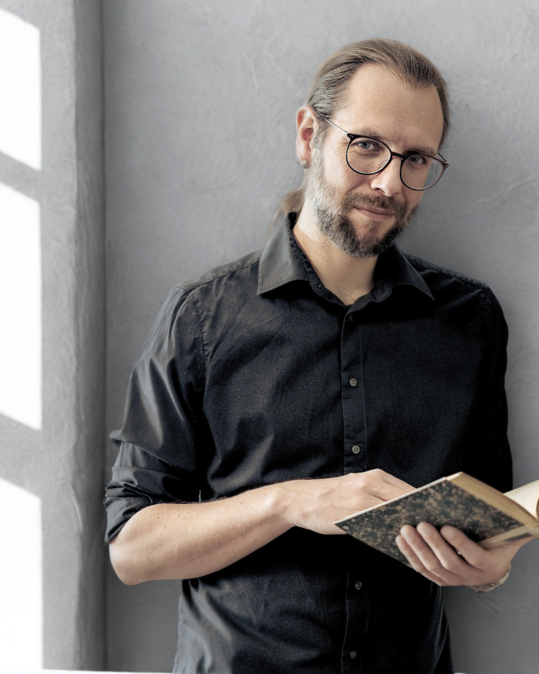 Mann in einem schwarzen Hemd, Brille und Buch in der Hand